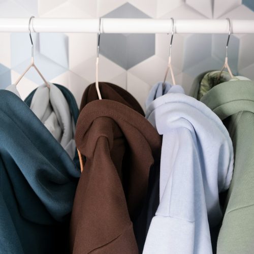 Row of multi-colored knitted hoodies, sports sweaters hanging on a hangers in an atelier or sportswe